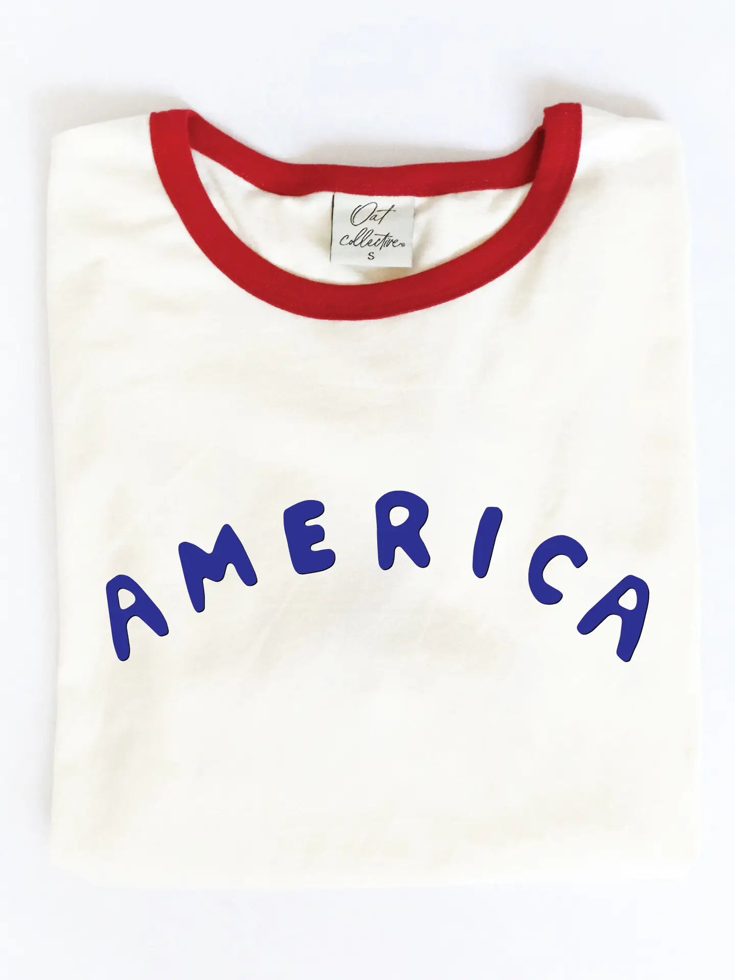 The Oat Collective America Puff Ringer Graphic T-Shirt features a white body, bold blue "AMERICA" puff print, red collar, and is crafted from premium Airlume cotton for comfort.