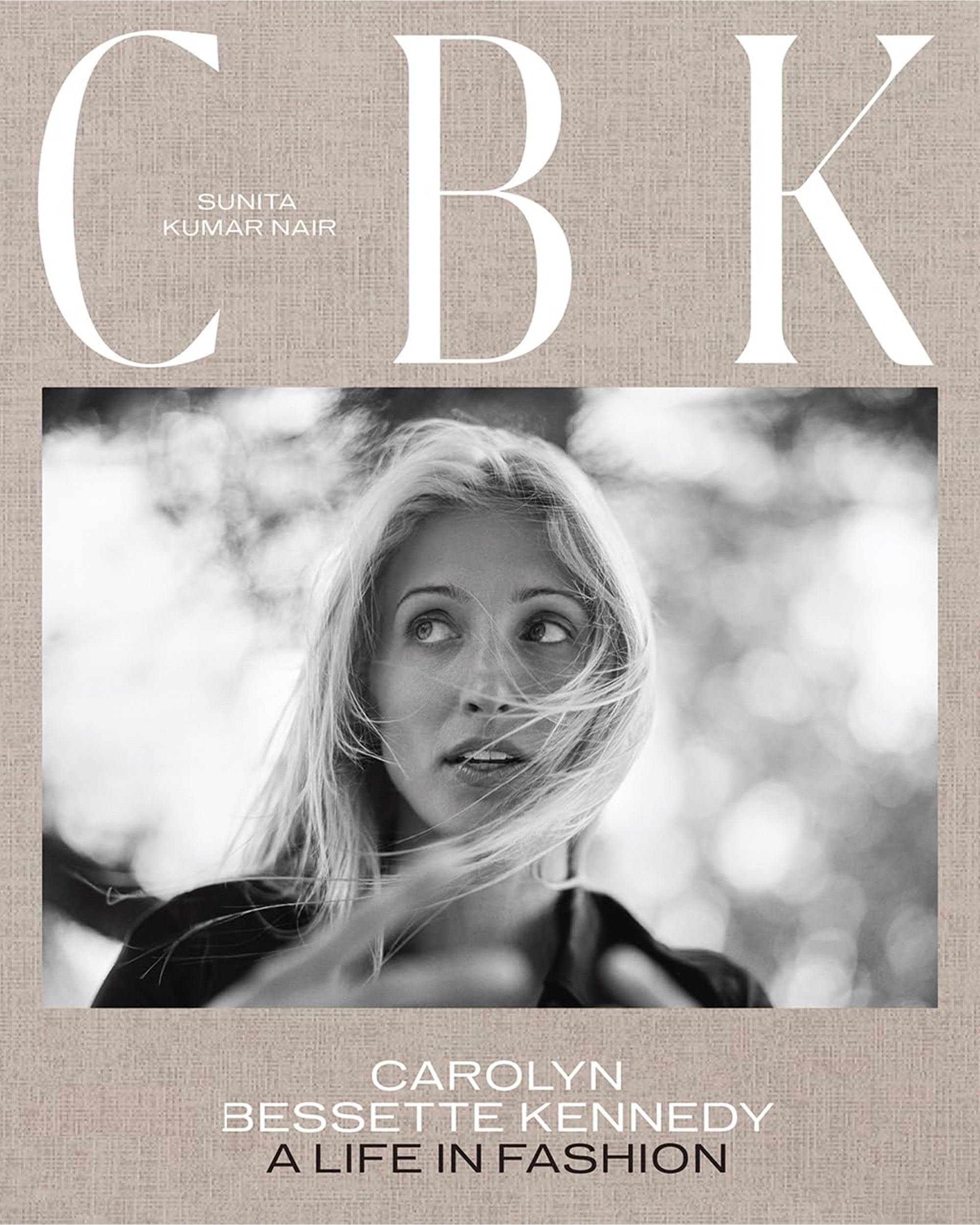 Black and white photo of a woman with windblown hair, framed by blurred branches. Text: “CBK: Carolyn Bessette,” Hachette Book Group. A tribute to the timeless style of this enduring fashion icon.