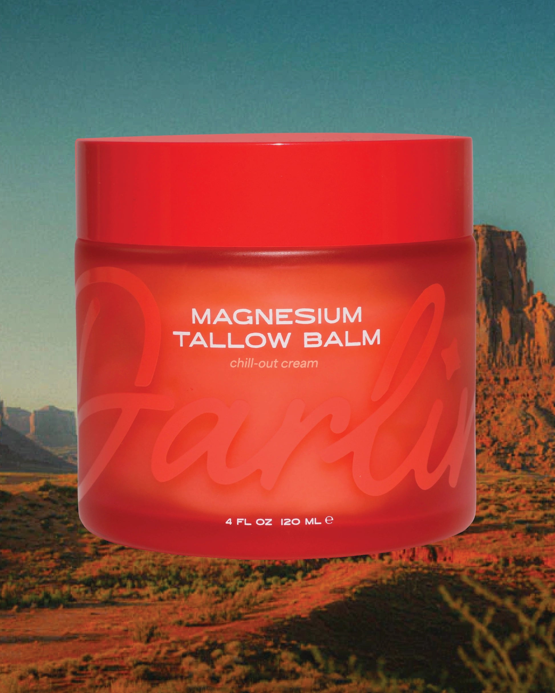 A red jar labeled "Magnesium Lavender Tallow Cream 4oz" by Faire is set against a desert with rocky formations and blue sky. The label features the brand name prominently, and the cream is infused with soothing lavender.