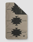 A gray rectangular SW Gray Towel by Faire, featuring a geometric black tribal pattern and a small "CAMP COZY" logo in the bottom right corner, is shown with the top right corner folded to reveal the reverse side.