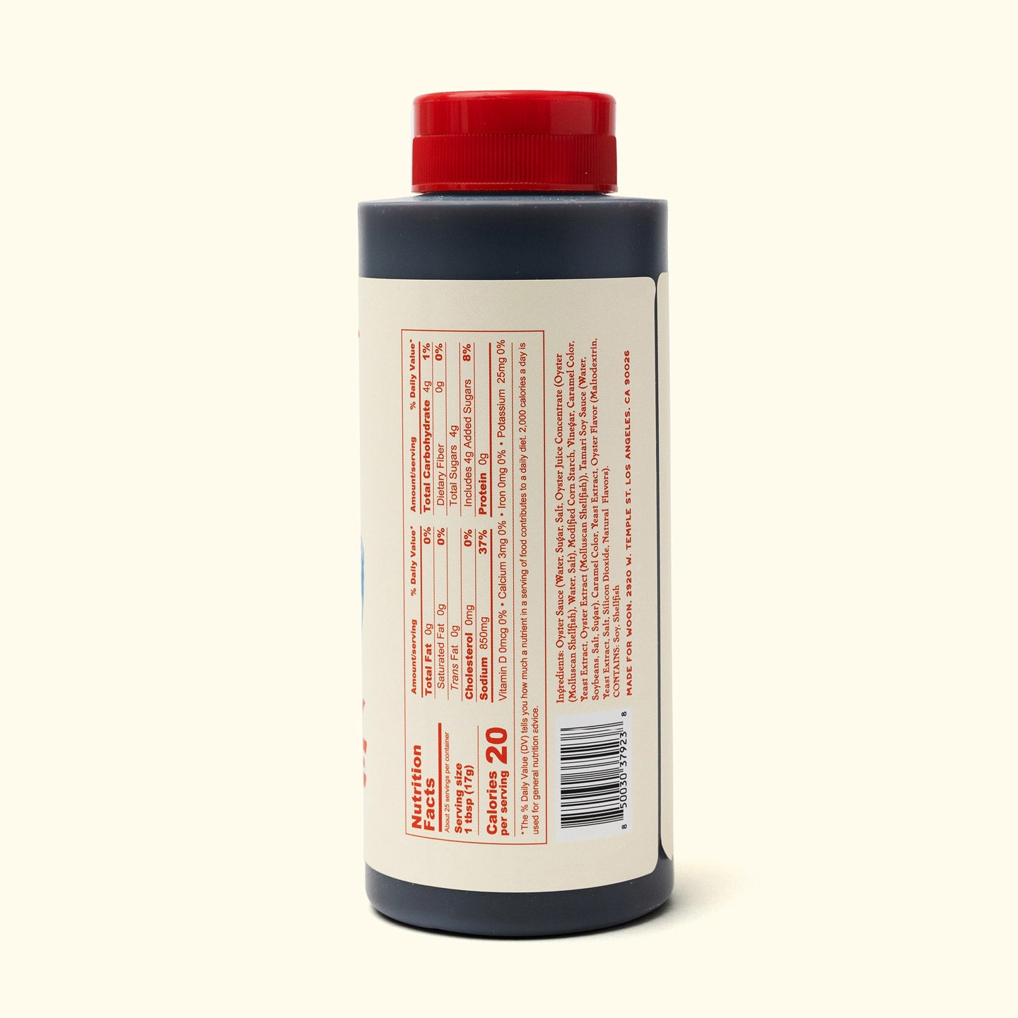 A plastic bottle of Faire Woon Stir Fry Sauce with a red cap and dark liquid stands upright on an off-white surface. The cream label with red text lists ingredients, nutritional info, and notes that it's a gluten-free cooking sauce.