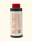 A plastic bottle of Faire Woon Stir Fry Sauce with a red cap and dark liquid stands upright on an off-white surface. The cream label with red text lists ingredients, nutritional info, and notes that it's a gluten-free cooking sauce.