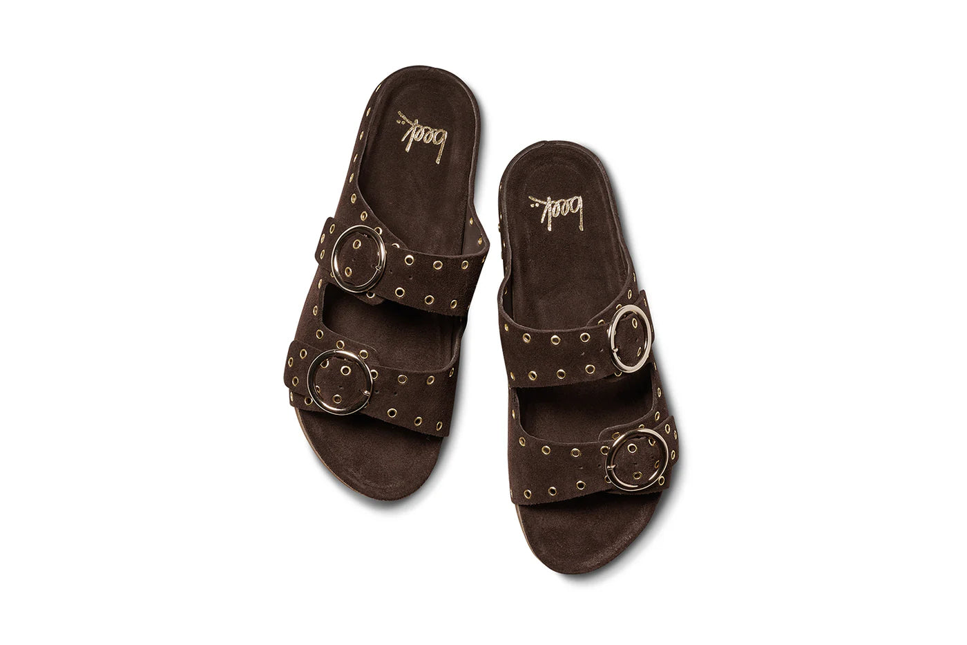 The Beek CEDAR sandals feature dark brown suede, two wide adjustable straps with large silver buckles and metal eyelet accents, a flat comfortable sole, and the brand name "Beek" printed on the insole.