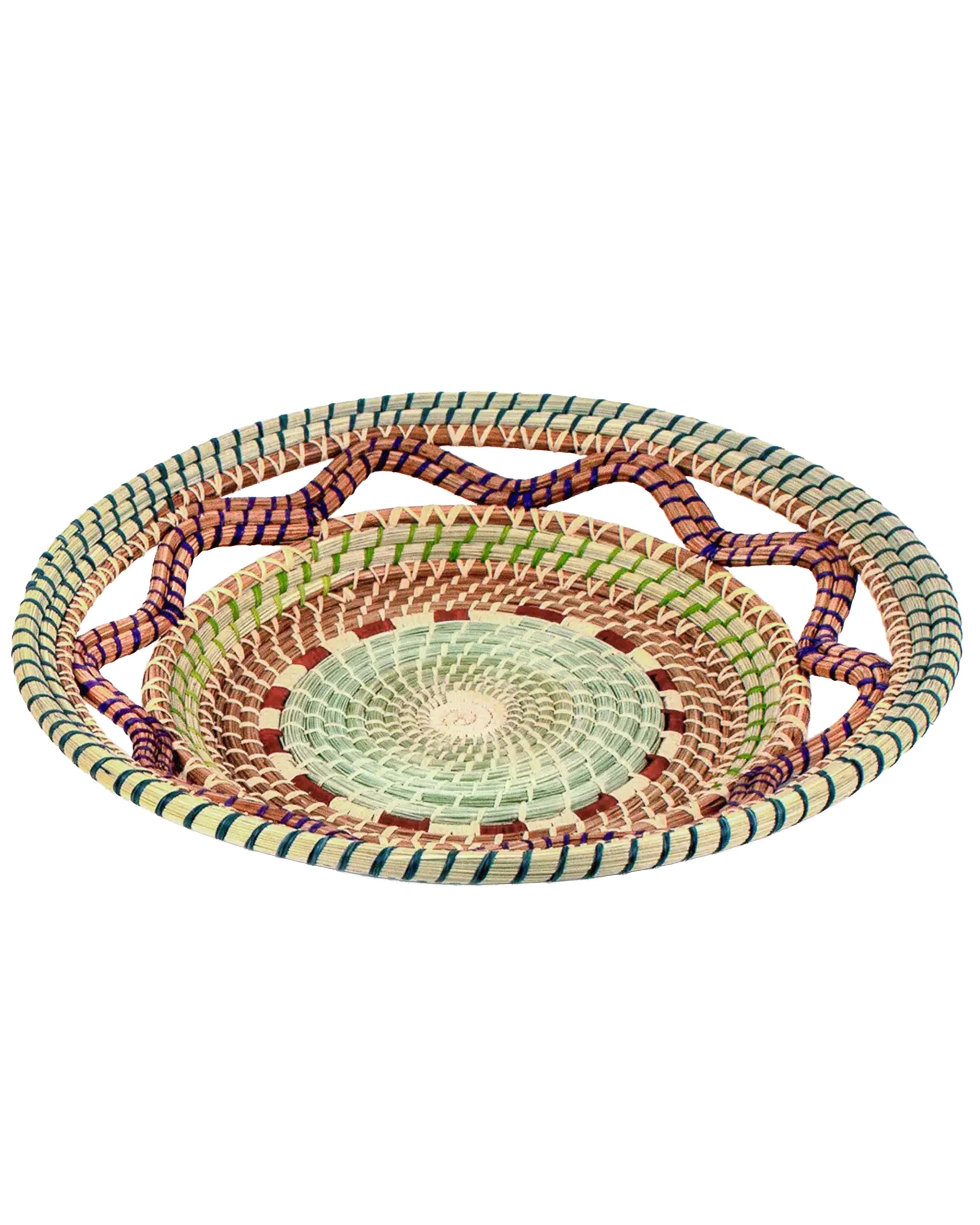The Celestina Basket by Faire is a shallow, round handcrafted pine needle basket with intricate beige, green, brown, and purple patterns, featuring a central spiral and a zigzag rim design.