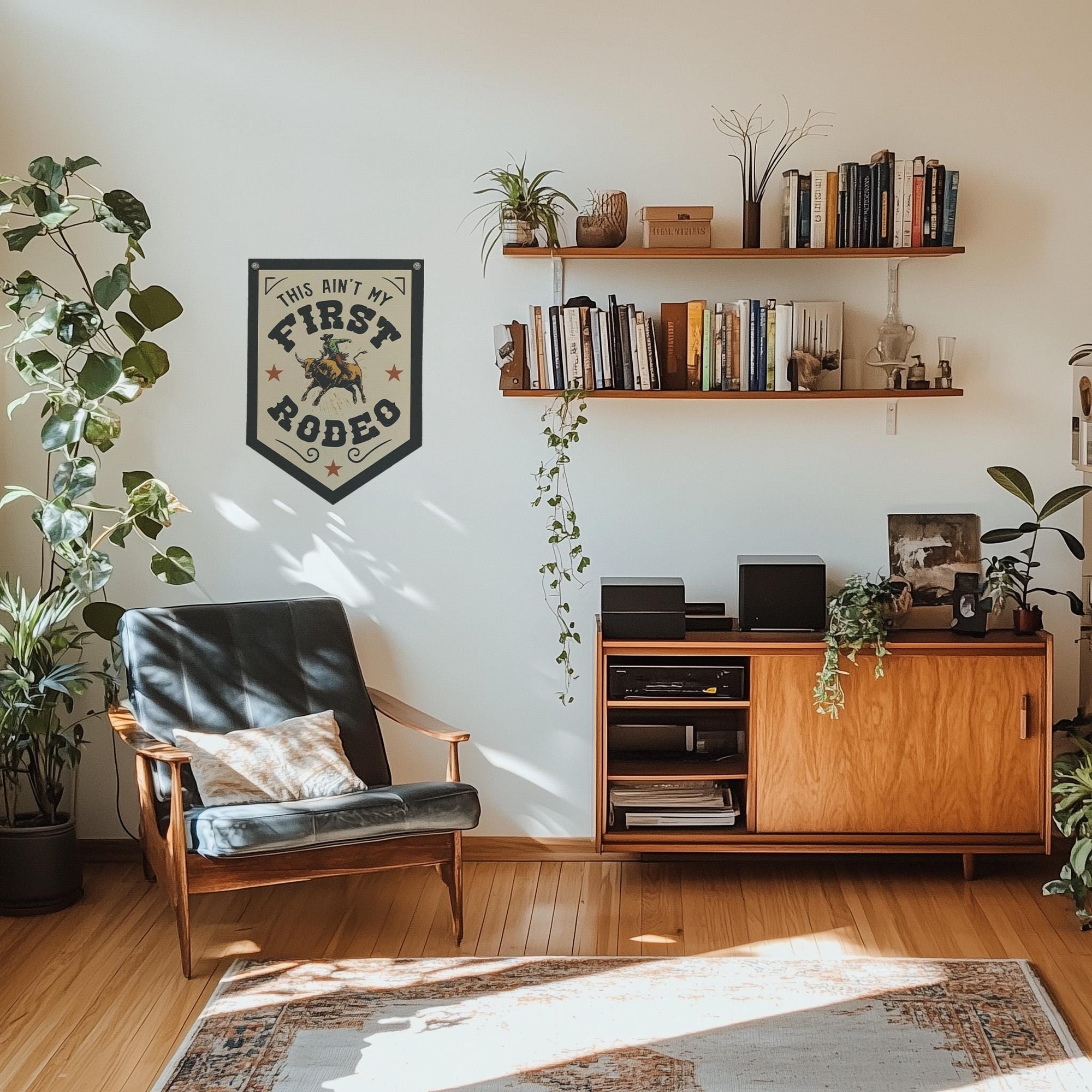 A cozy living room with wooden floors, a Faire mid-century armchair, bookshelves, potted plants, and a vintage "Ain't My First Rodeo" banner on the wall. Sunlight streams through the window.