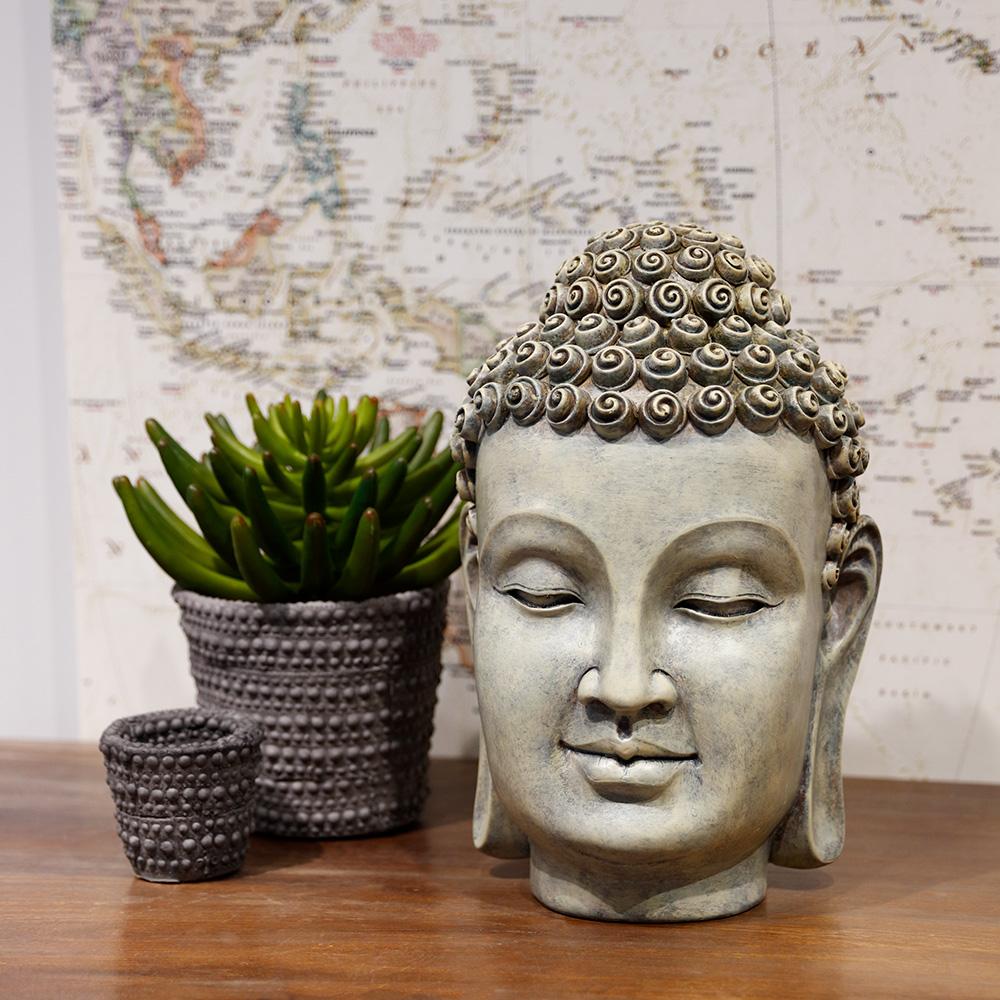 The Aeonium in Cement Pot by AllState Floral And Craft sits beside a decorative Buddha head statue and a matching cup on a wooden surface, with a map backdrop, creating a serene and balanced arrangement.