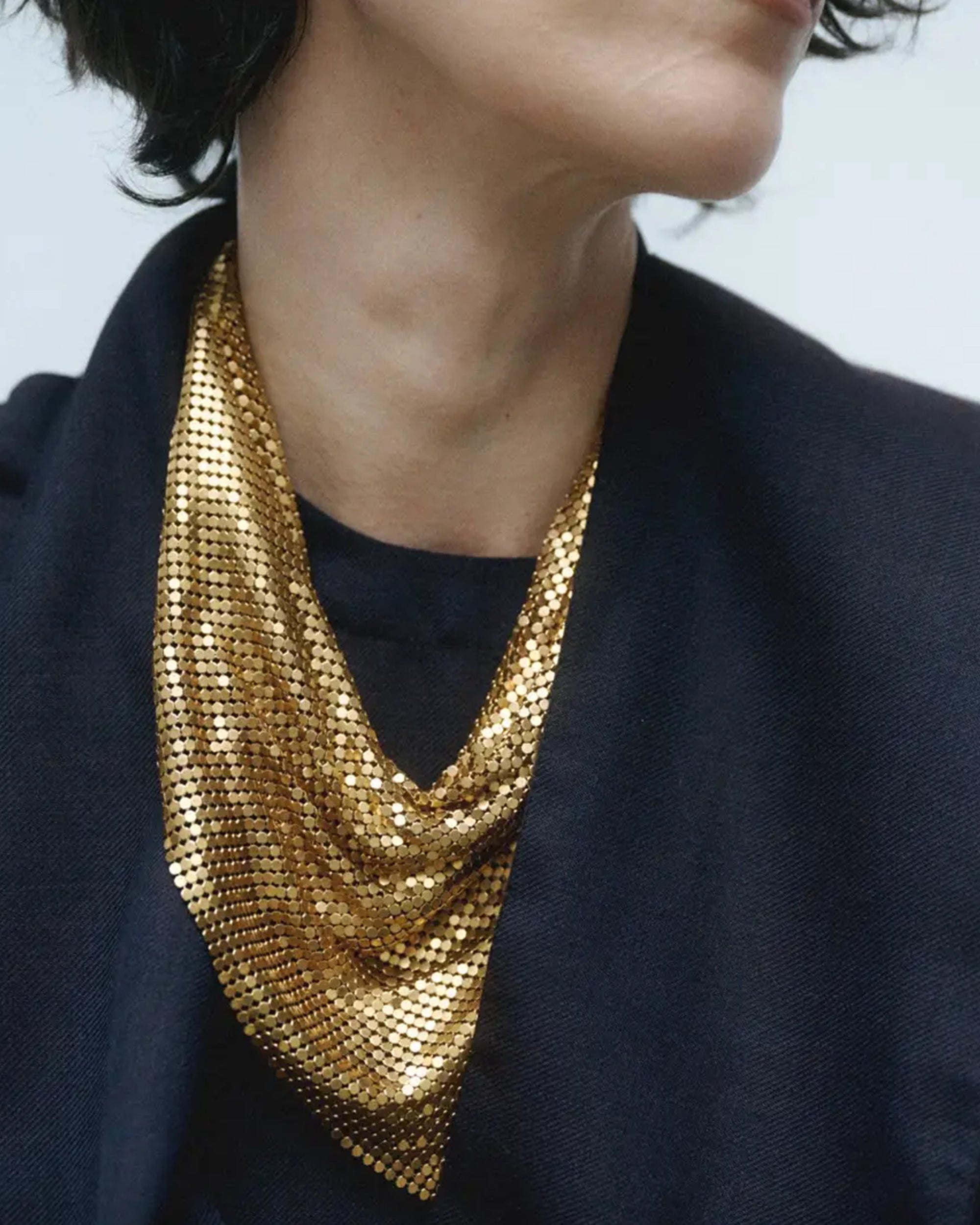 A person in a dark top wears the Faire Chain Mail Bandana Scarf Necklace draped stylishly around their neck. Their face is partially out of frame.