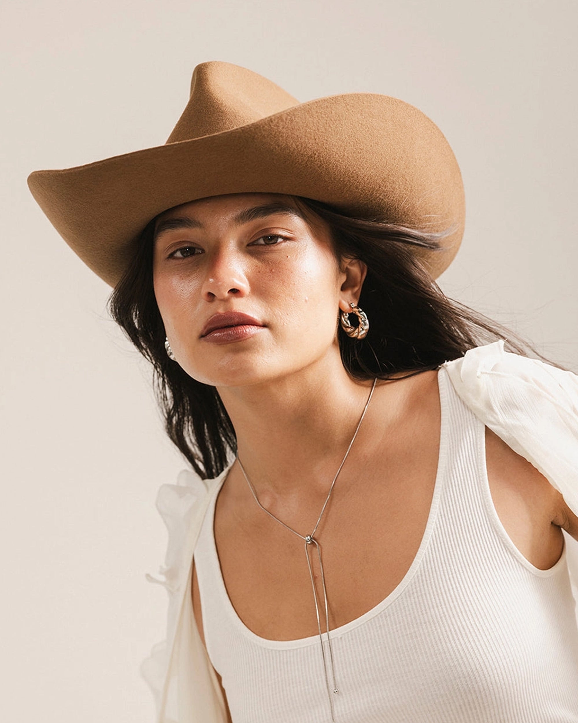 A woman models the Faire Charlie Western Hat, paired with a white tank top, hoop earrings, and a long necklace, looking calmly at the camera against a neutral background.