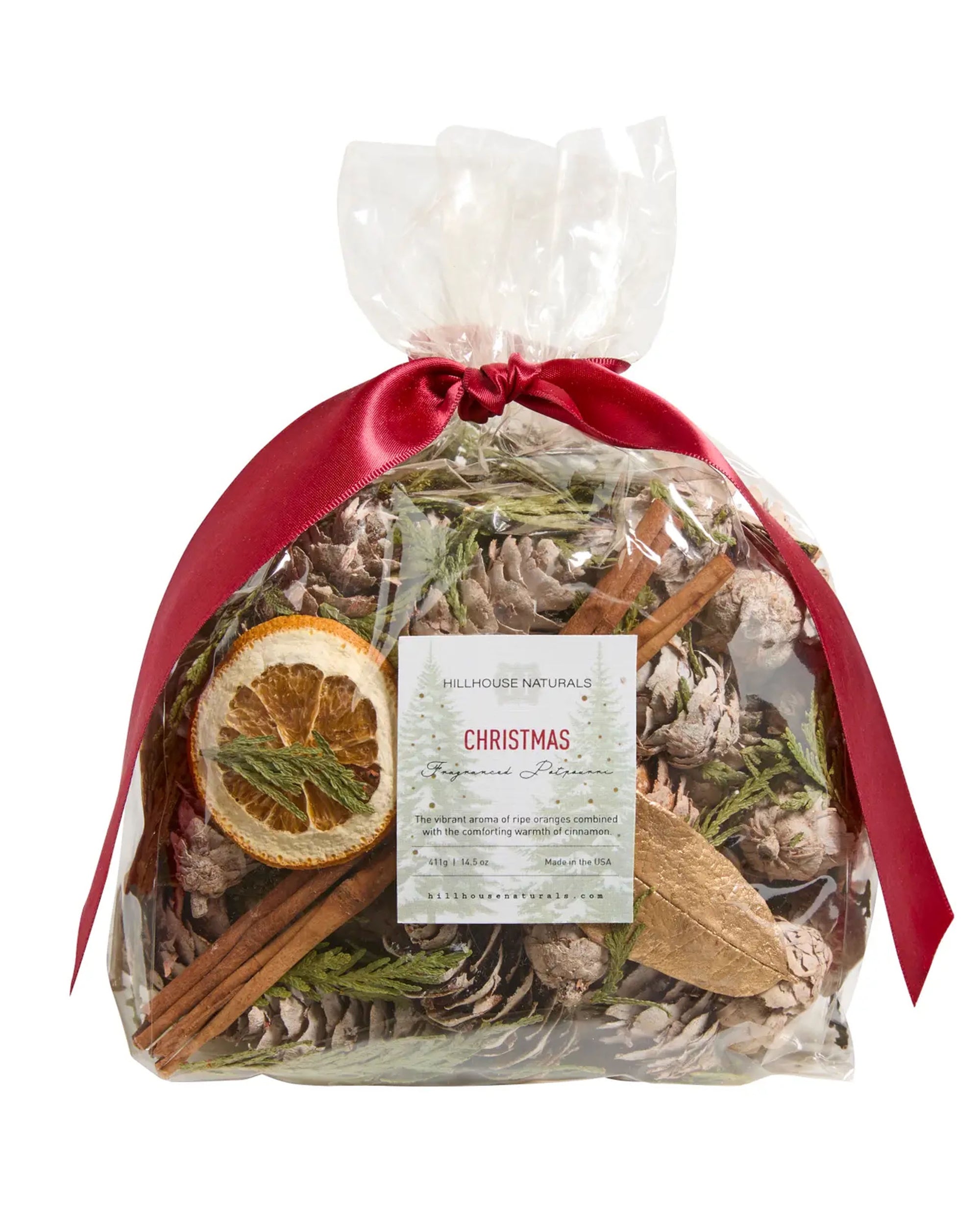 A clear bag of Faire Potpourri with pinecones, greenery, dried orange slice, and cinnamon sticks, tied with a red ribbon. Fill your home with classic holiday scents of balsam and pine this Christmas season. Label reads "Faire Potpourri.