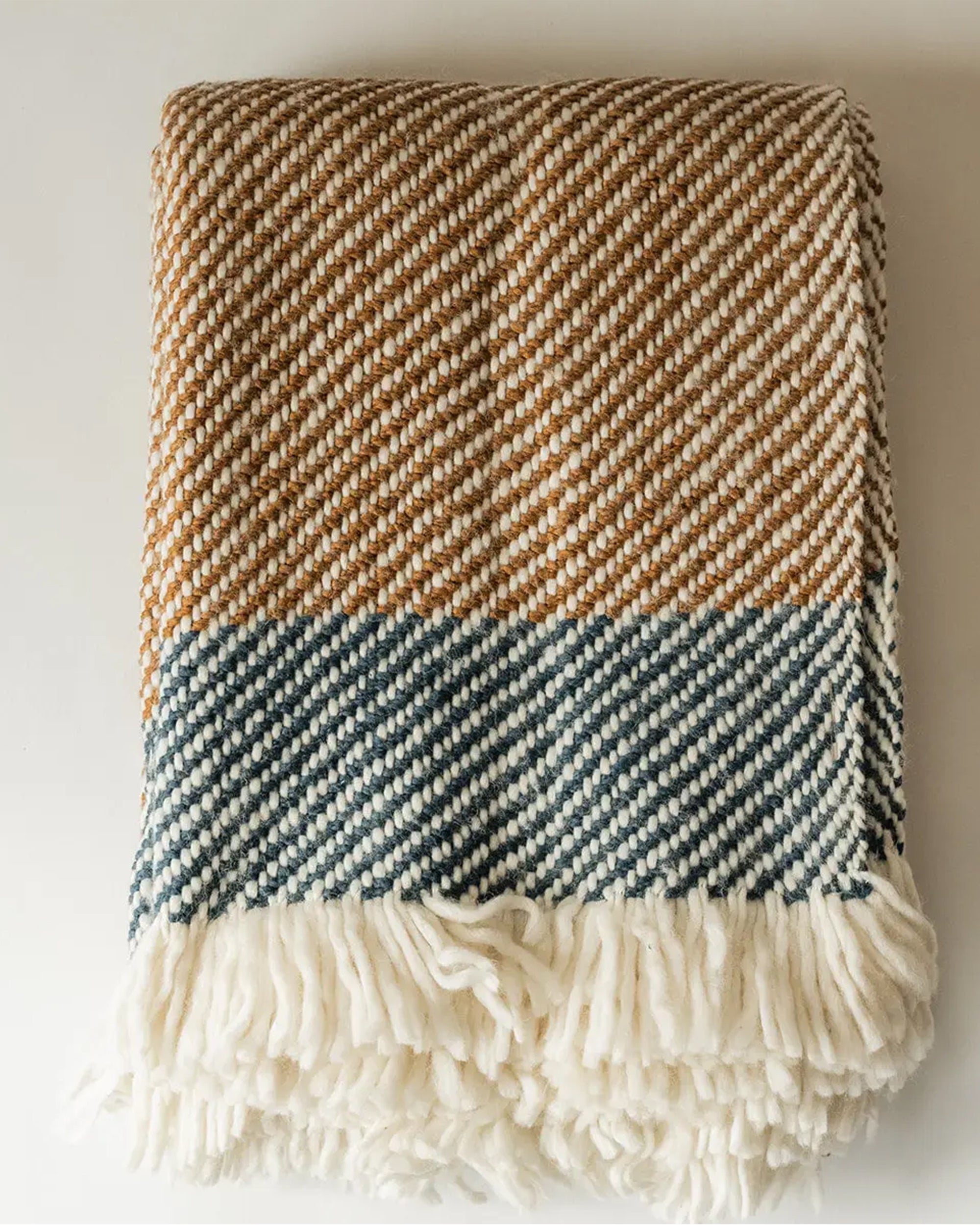 The Faire Chunky Twill Throw, with brown and blue diagonal stripes and a thick cream fringe along the edge, is folded and displayed on a white surface.
