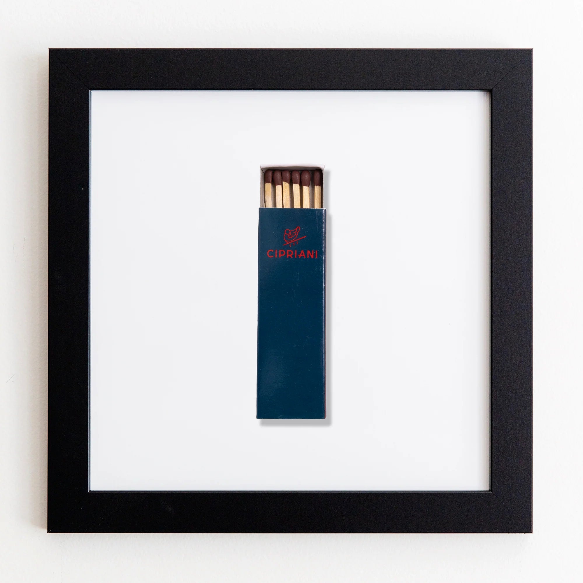 A framed artwork featuring a matchbox labeled &quot;Cipriani&quot; containing several matches, centered on a white acrylic background within a Art Square Black Frame from Match South.