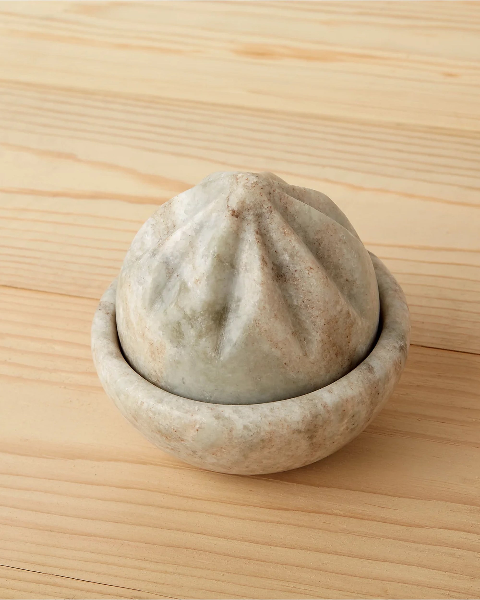 The Be Home Waterfall Marble Citrus Press, featuring a hand-finished ridged conical top and shallow bowl base, rests on a light wooden surface.