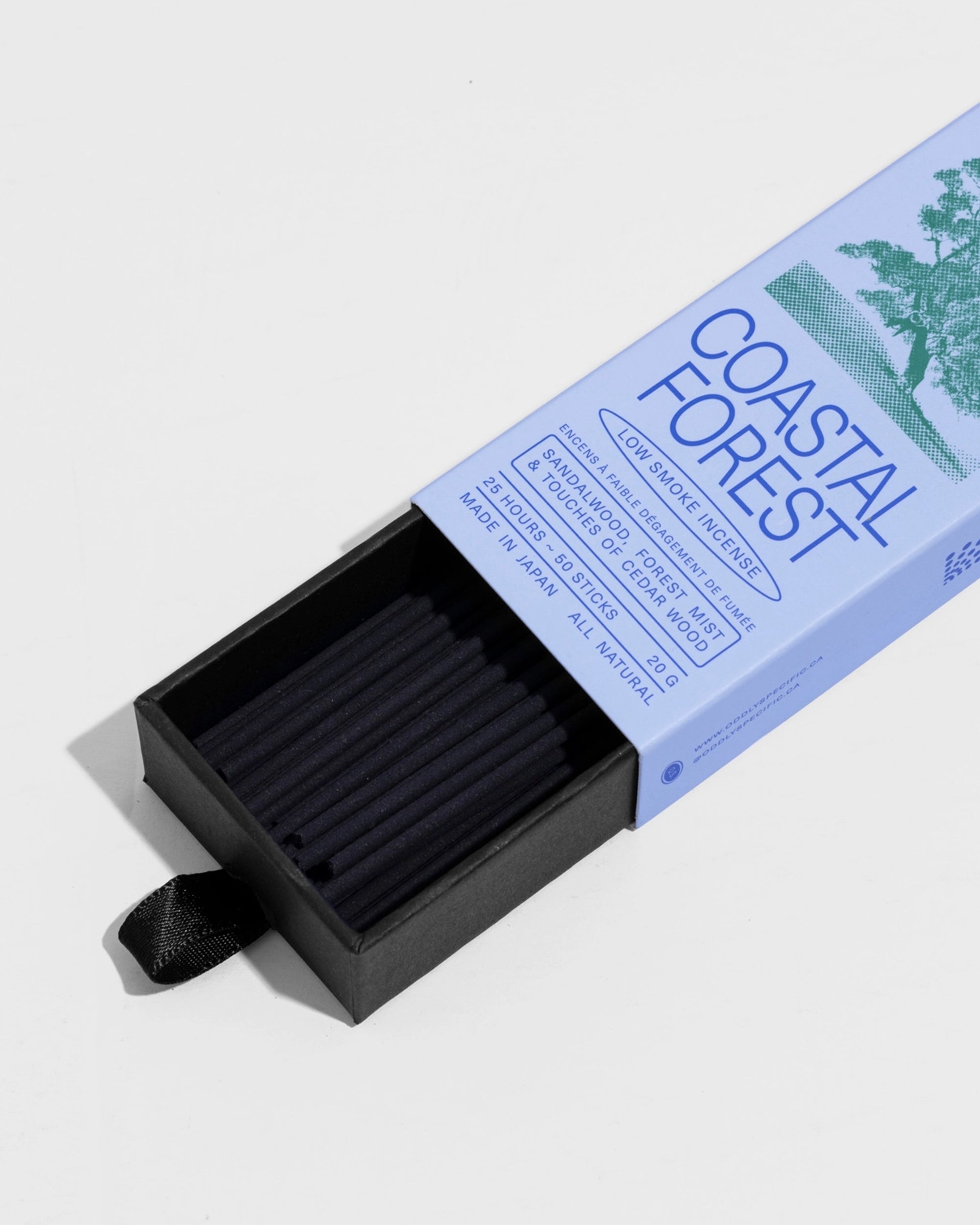 A box labeled "Coastal Forest" by Faire contains neatly arranged black sandalwood Low Smoke Incense sticks, partially pulled out with a black ribbon. The packaging highlights natural ingredients and describes the incense as gentle and refined.