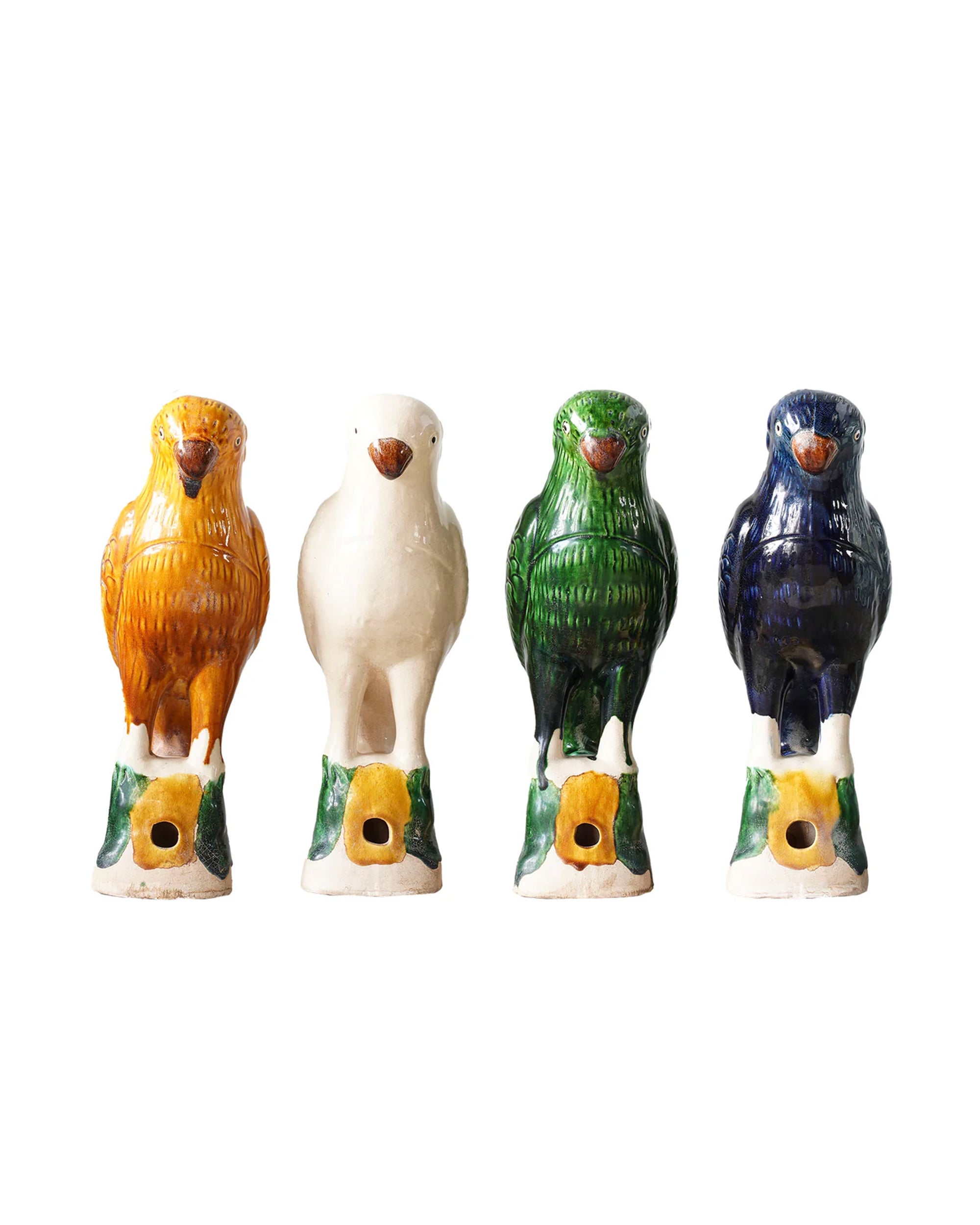 Four Parrot Small whistles by Blue Ocean Traders stand in a row in orange, white, green, and dark blue colors on green and yellow bases with a front hole—evoking Jingdezhen hand-painted porcelain artistry.