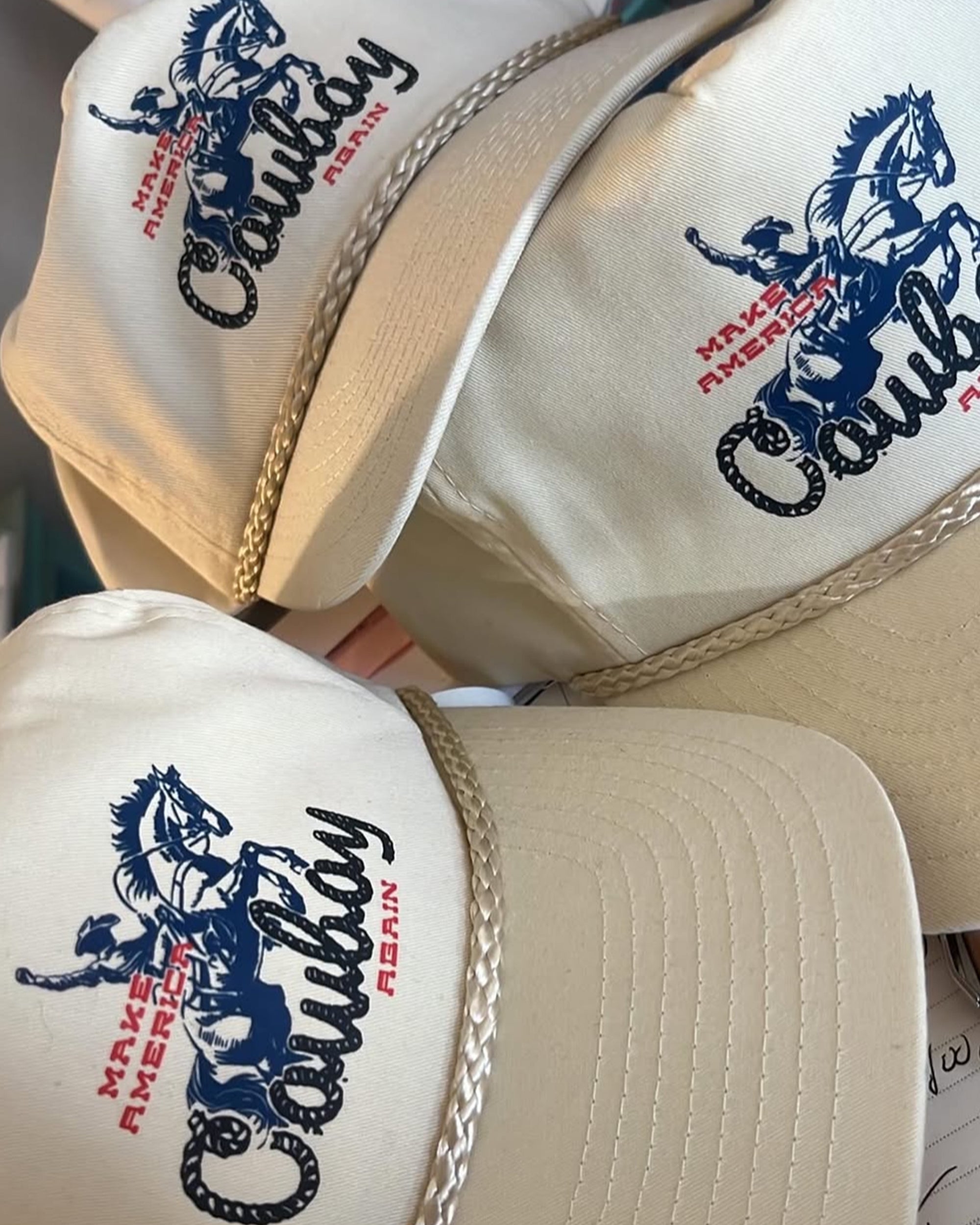 Three beige Make America Cowboy Again caps by Ping Pong Surf Club feature braided brims, a country style cowboy and horse graphic, and bold blue and red "MAKE AMERICA COWBOY AGAIN" text.
