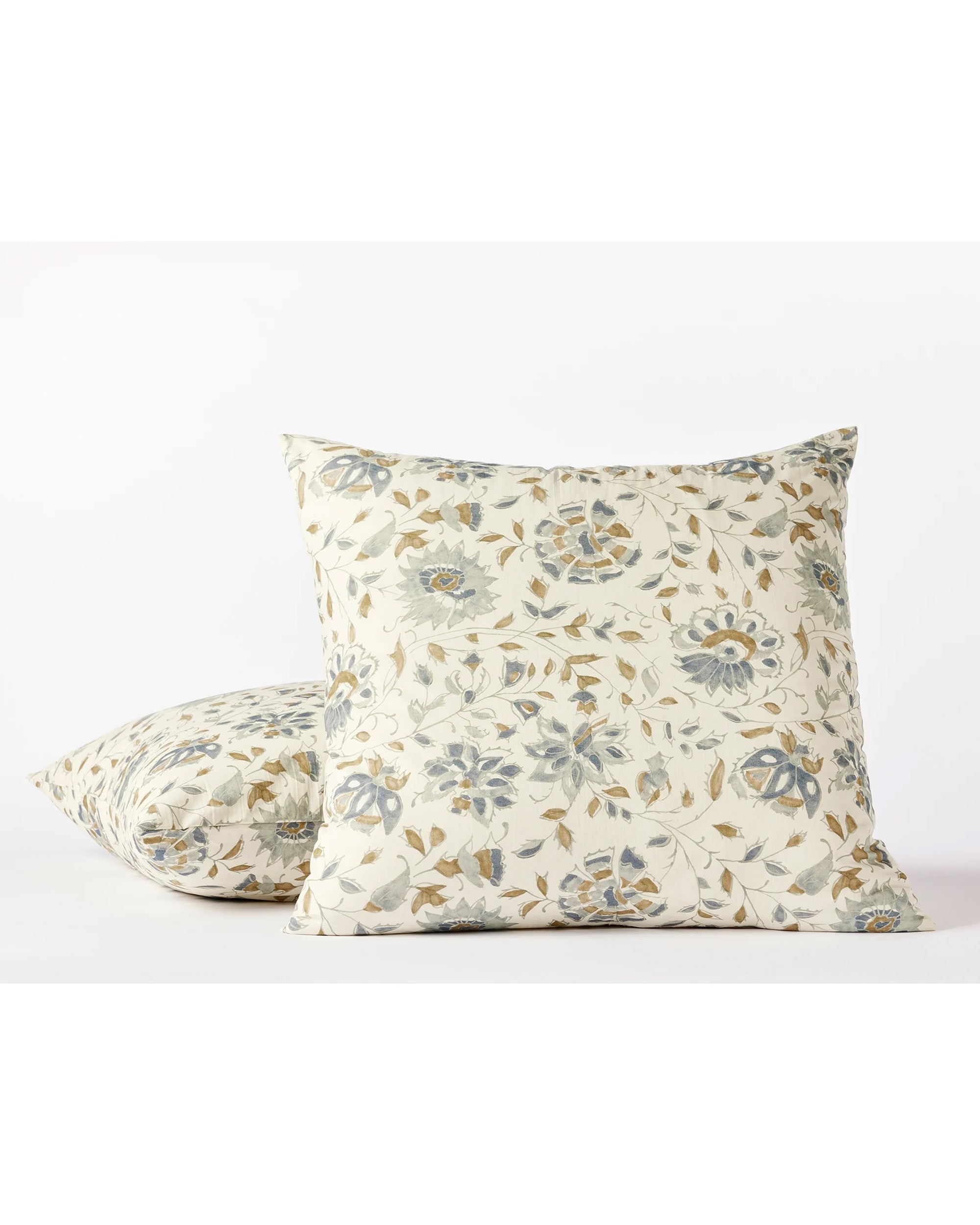 Two Coyuchi Inc Flora Org Print Sham Undyed Lagoon Euro shams—square, made of organic cotton percale, featuring a subtle botanical motif in blue, beige, and green on a white background. One sham stands upright; the other lies flat behind it.