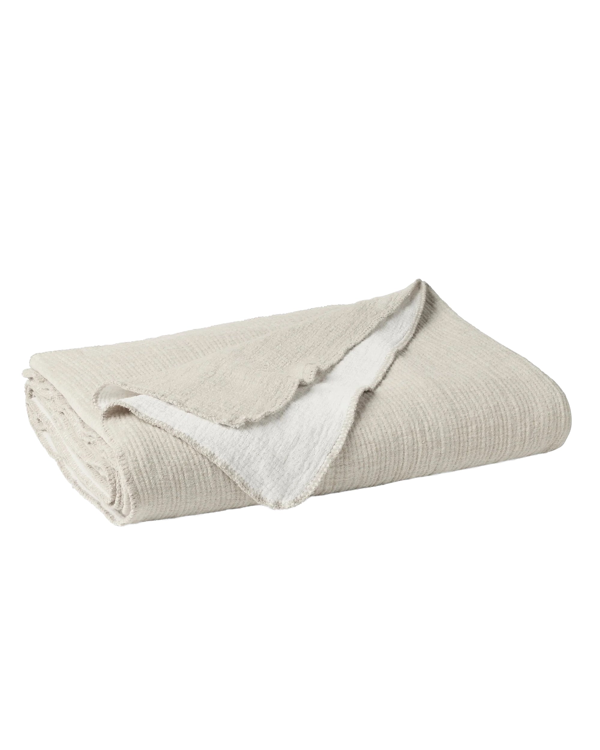 The Cozy Cotton Org. Blanket by Coyuchi Inc is a beige, reversible organic cotton chenille blanket with a soft, textured surface and white inner lining, shown partially turned over against a plain white background.