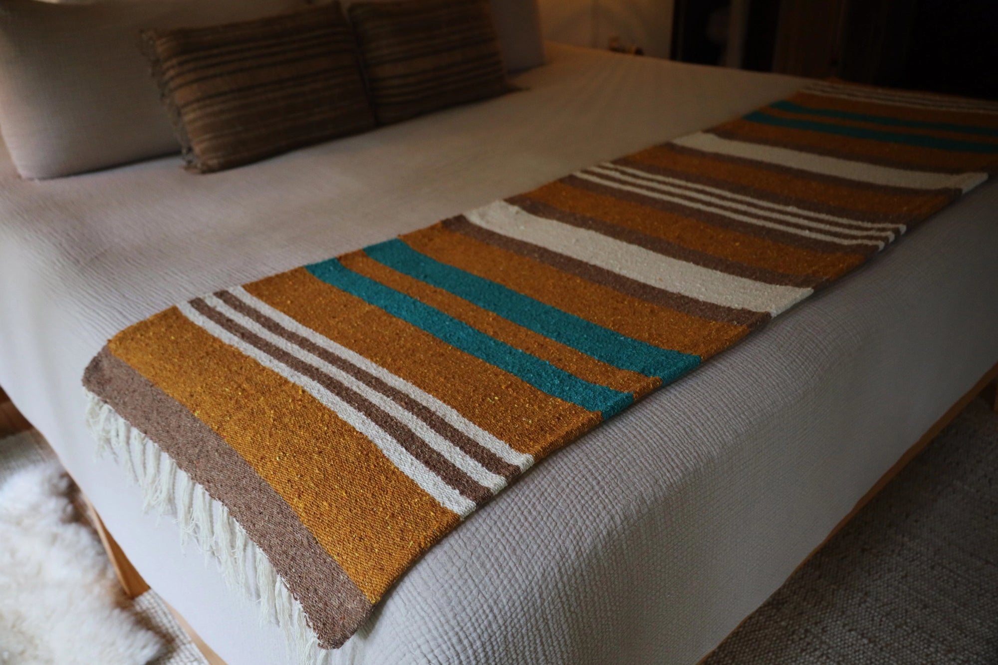 Handwoven striped blanket in brown, gold, teal, and white on bed; Bungalow Furniture &amp; Accessories.