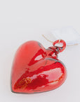 The Glass Heart Medium by Faire is a handcrafted, glossy, red glass heart-shaped ornament that evokes Mexican tradition. It rests on a white surface and features a string with a white tag.