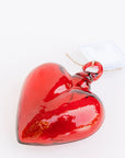 The Faire Glass Heart Small ornament is a glossy red blown glass piece with a top loop and an attached tag, reminiscent of rich Mexican tradition. This handcrafted ornament is beautifully reflective and elegantly displayed against a plain white background.