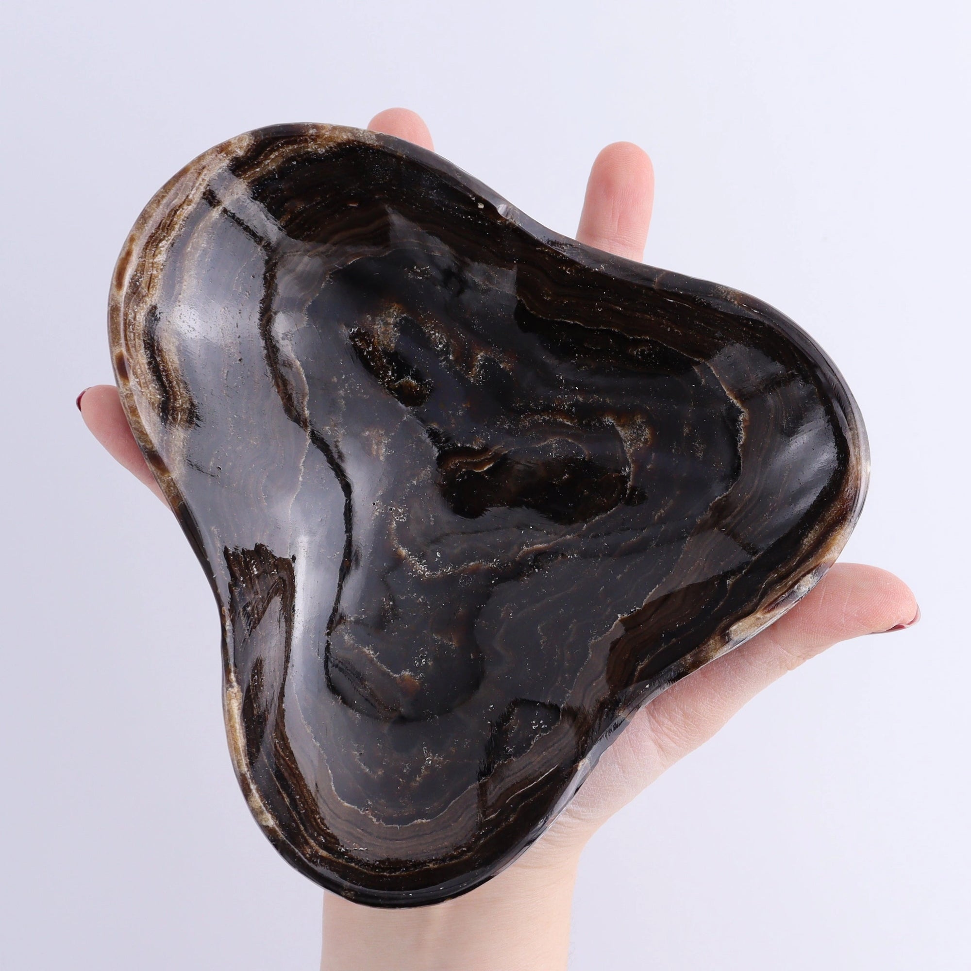 Triangular Mexican onyx and calcite bowl in dark chocolate hues, held by hand; Faire.