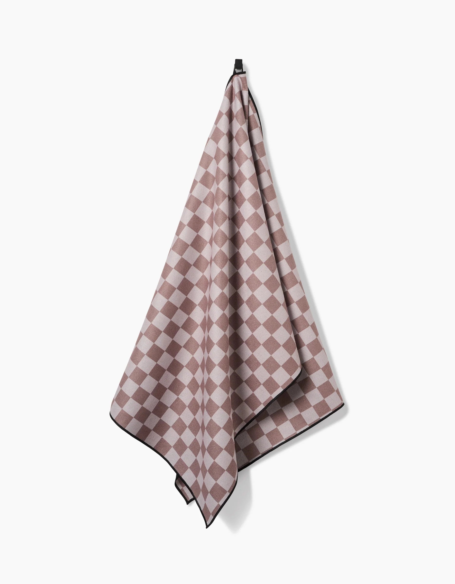 The Faire Chic Checker Yoga Towel in pink and beige checkered pattern with black trim hangs from a hook against a plain white background.