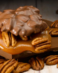 A cluster of LC Longhorns Chocolate 1.5oz by Faire—pecan caramel candy covered in milk chocolate—rests on a wooden surface amid whole pecans, offering an authentic Texas treat.