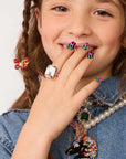 Adorned with the Faire "Days of The Week" press-on nail kit and a stylish clear ring, a young girl in denim beams. Her look features a pearl necklace, a jewel-encrusted horse pendant, and is finished with a playful butterfly hair clip.