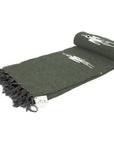 The Olive Green Baja Thunderbird Blanket by Faire features white horse and rider designs, black fringe, and a small fabric tag—handmade in Mexico and perfect for yoga.