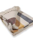 The Frontier Cotton Throw by Faire features brown, navy blue, and mustard yellow horizontal stripes with cream fringed edges on a cream background. Made from 100% cotton, it's shown folded against a white surface.