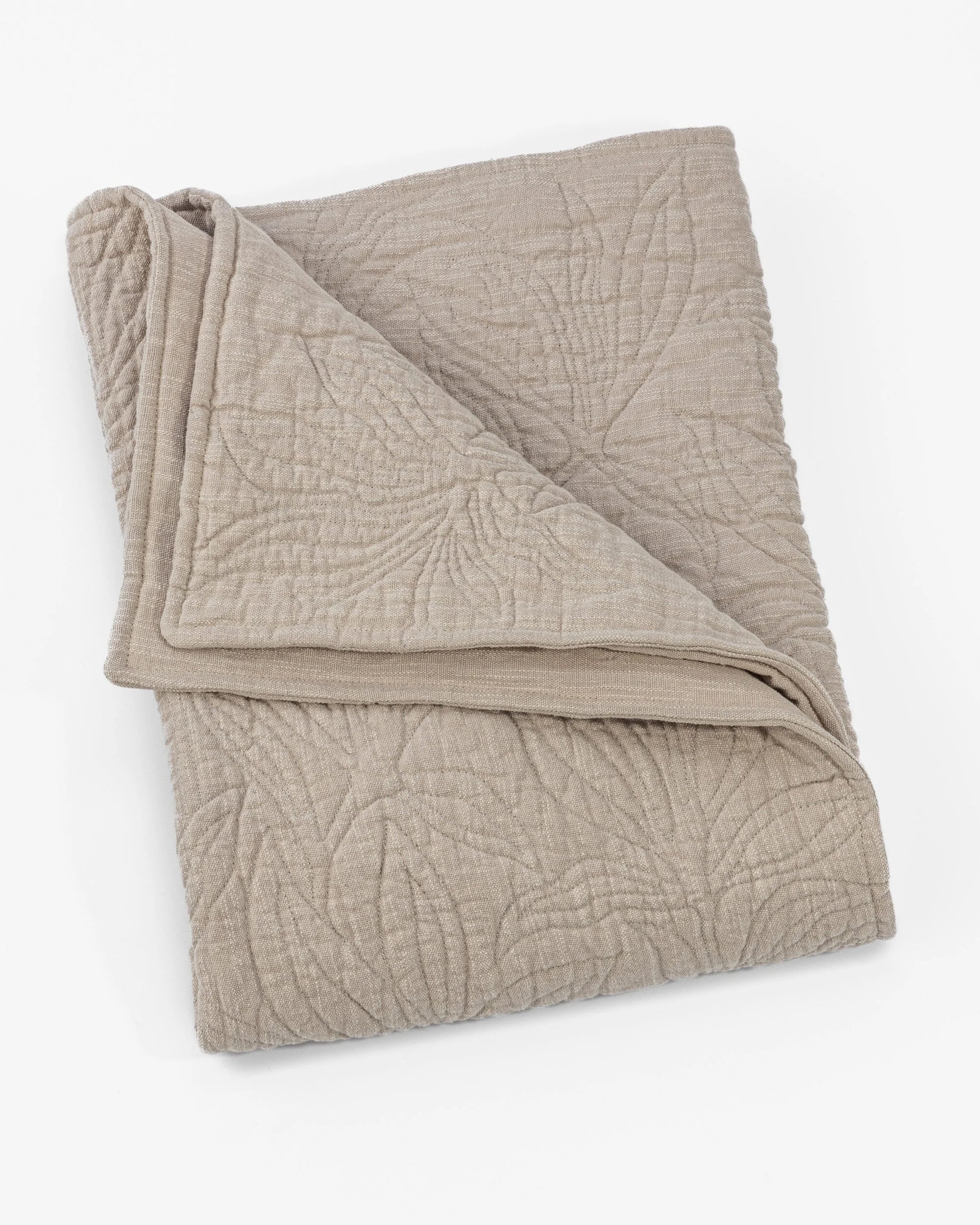 The Amity Home Davina Quilt Queen, in beige, showcases traditional elegance with a subtle stitched leaf pattern and floral quilting, neatly folded against a white background.