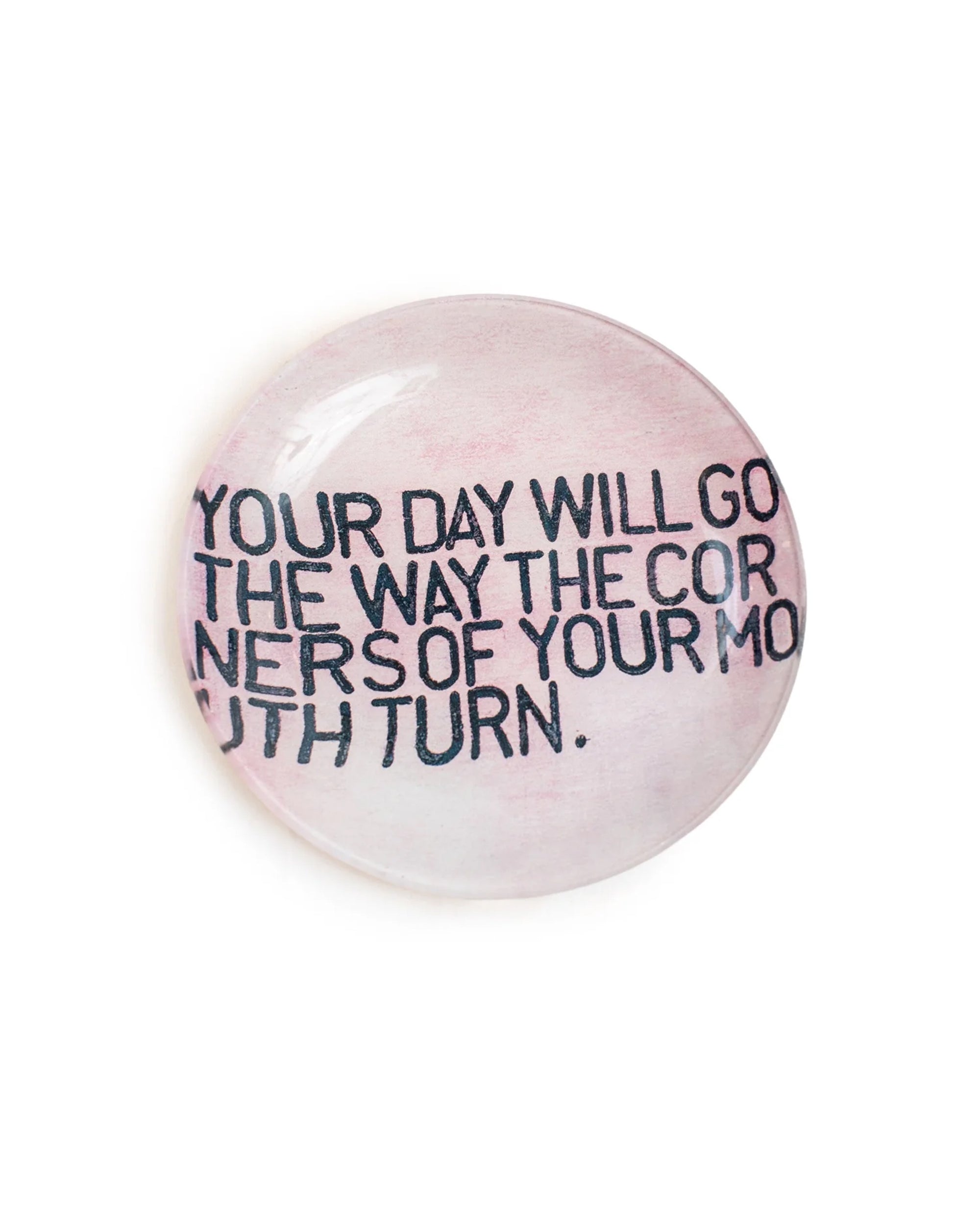 The Sugarboo Designs "Your Day Will Go Round Plate" features black text saying "YOUR DAY WILL GO THE WAY THE CORNERS OF YOUR MOUTH TURN" on a light pink background. Perfect as a jewelry holder or decor with art prints.