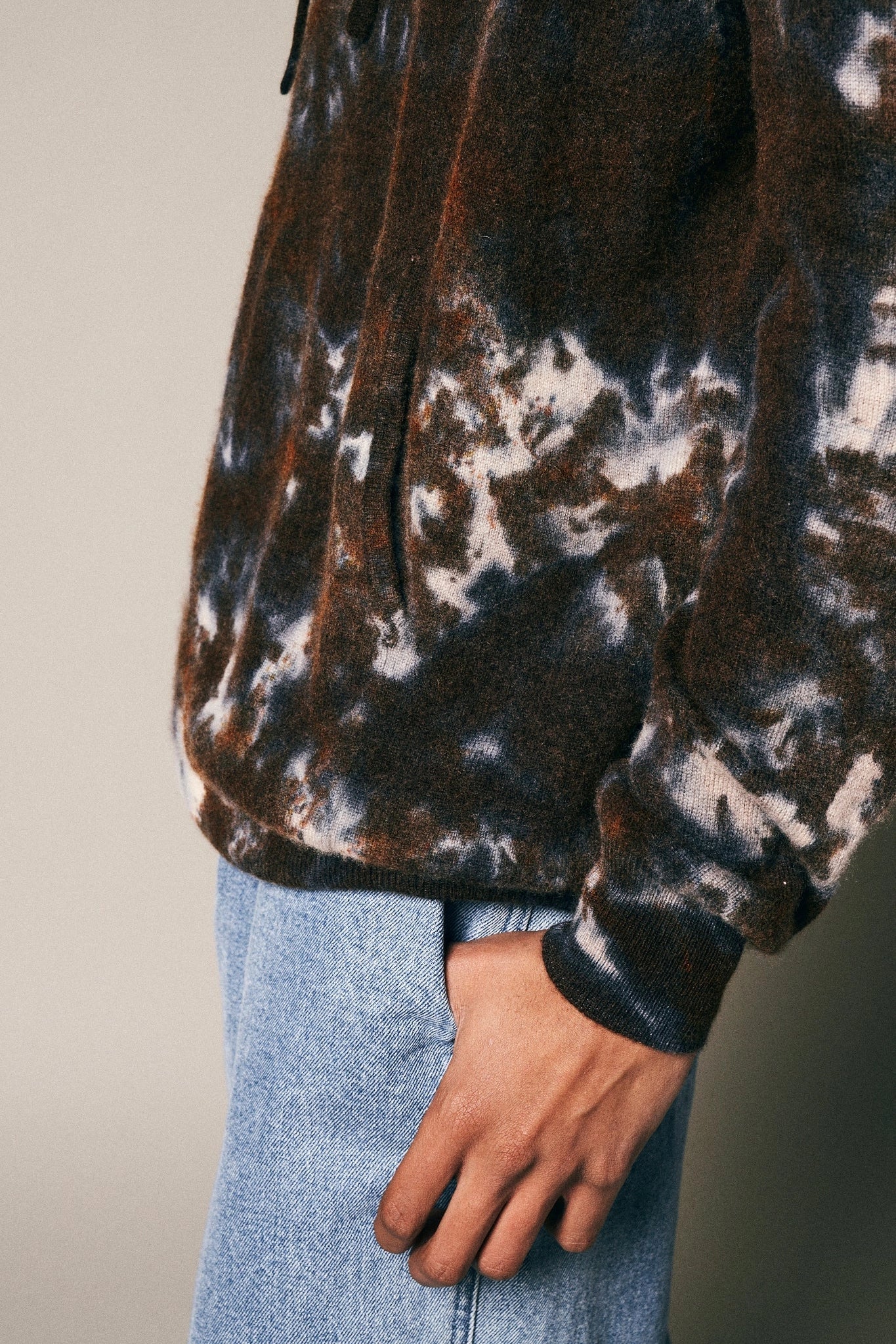 A person models the Riverside Tool & Dye Cashmere Hoodie in brown and white against a neutral background, wearing light blue jeans. Only their torso, part of one arm, and hand resting by their side are visible.