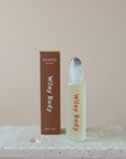 A Wiley Roller, ideal for aromatherapy and wellness, is displayed next to its packaging. The transparent bottle has a metal applicator, and the brown box with white text is placed on a textured stone surface against a calming beige background.