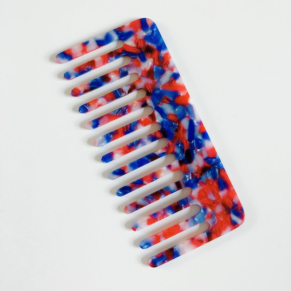 The Faire Hair Comb Assorted, featuring wide teeth and an anti-static design with a marbled red, blue, and white pattern, is shown on a plain white background.
