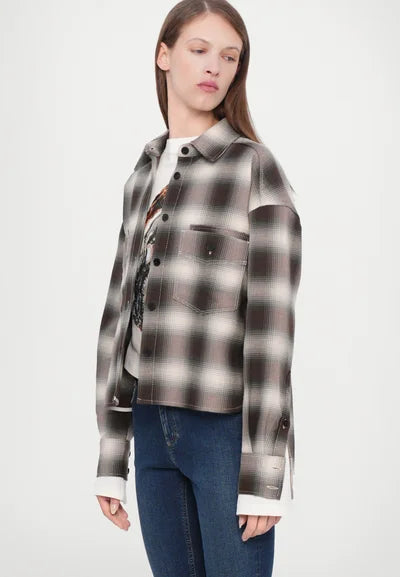 A person in the CLOSED Cropped Front OS Shirt—a black, white, and gray checkered cotton shirt with a chest pocket—layered over a graphic tee and blue jeans, stands against a light background, looking to their left.
