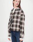 A person in the CLOSED Cropped Front OS Shirt—a black, white, and gray checkered cotton shirt with a chest pocket—layered over a graphic tee and blue jeans, stands against a light background, looking to their left.