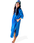 A woman stands barefoot on a white background, wearing the Faire Surf Stripe Shirt Dress and a "SURF" cap, with one hand in her pocket and a smile on her face.
