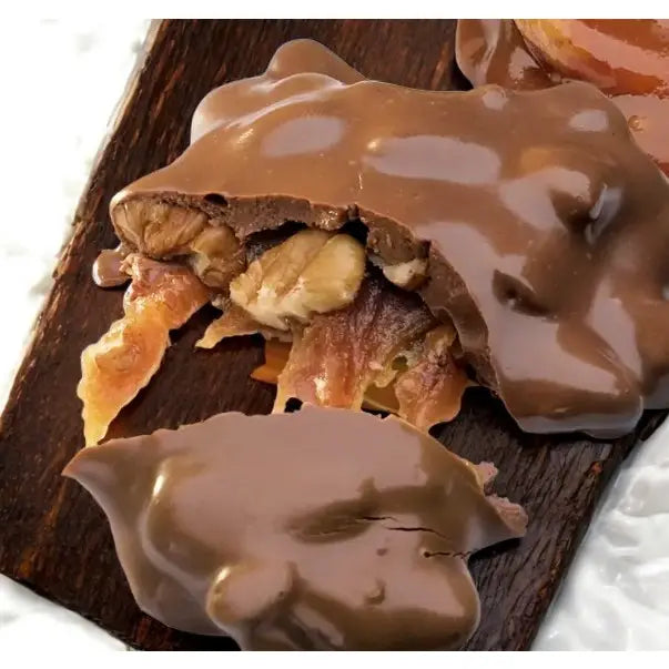 Close-up of a Faire LC Longhorns Chocolate 1.5oz candy, with a broken piece showing pecans and caramel inside, resting on a dark wooden surface.