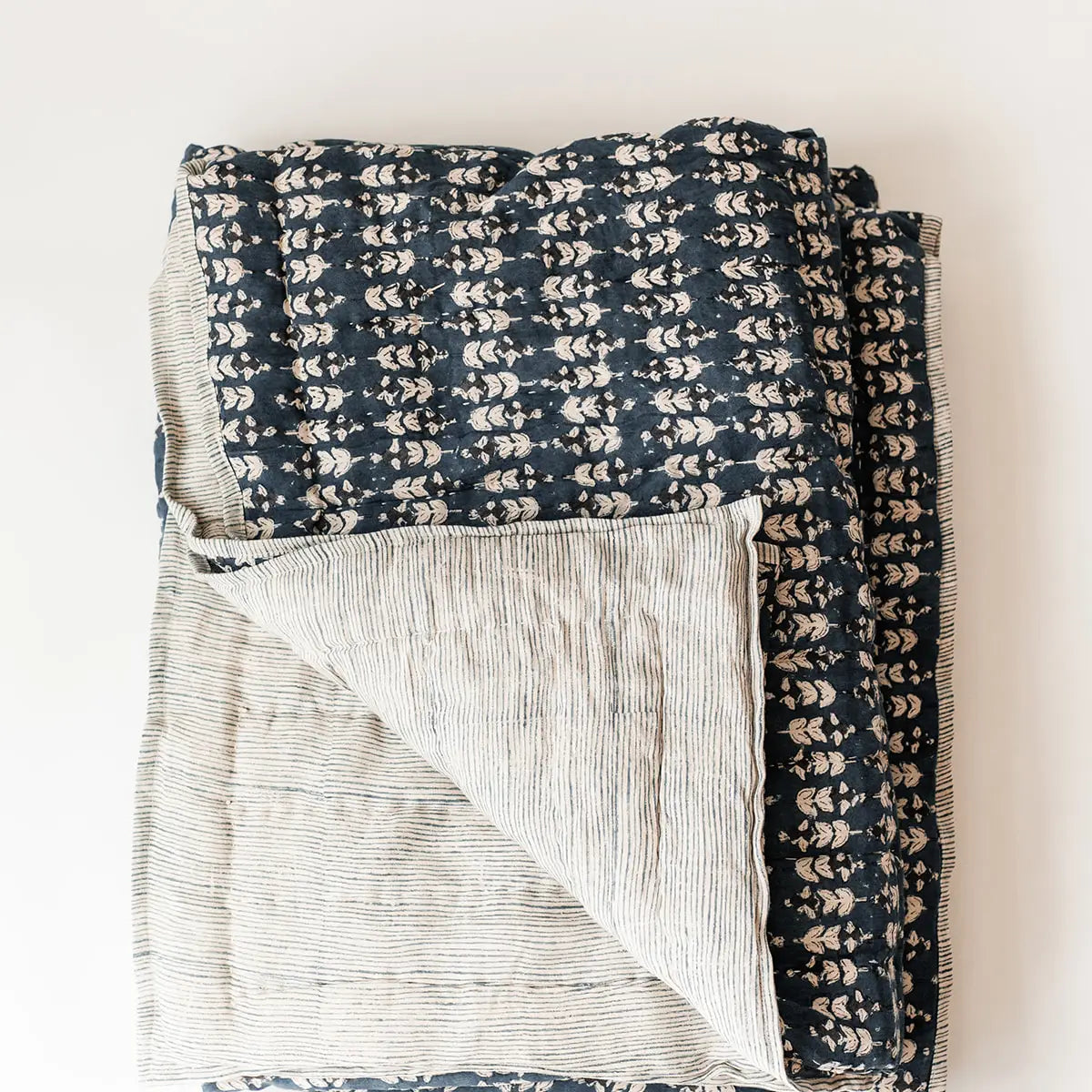 The Faire Blossom Block Print Blanket features a navy floral design on one side and thin beige-blue stripes on the other—handcrafted and ideal for bringing bohemian charm to your bedding.