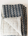 The Faire Blossom Block Print Blanket features a navy floral design on one side and thin beige-blue stripes on the other—handcrafted and ideal for bringing bohemian charm to your bedding.