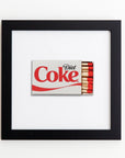 A framed acrylic art piece depicting a Match South matchbook with a Diet Coke logo. The matchbook features a red-tipped matchstick design along one side, against a white backdrop, displayed in an Art Square Black Frame.