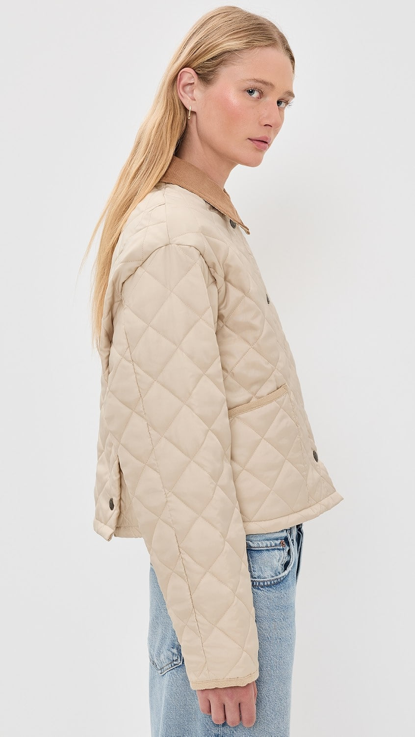 A woman with long blonde hair models the Denimist FAULKNER QUILTED JACKET, a beige lightweight jacket with snap closures, and light blue jeans, shown in a side pose against a plain white background.