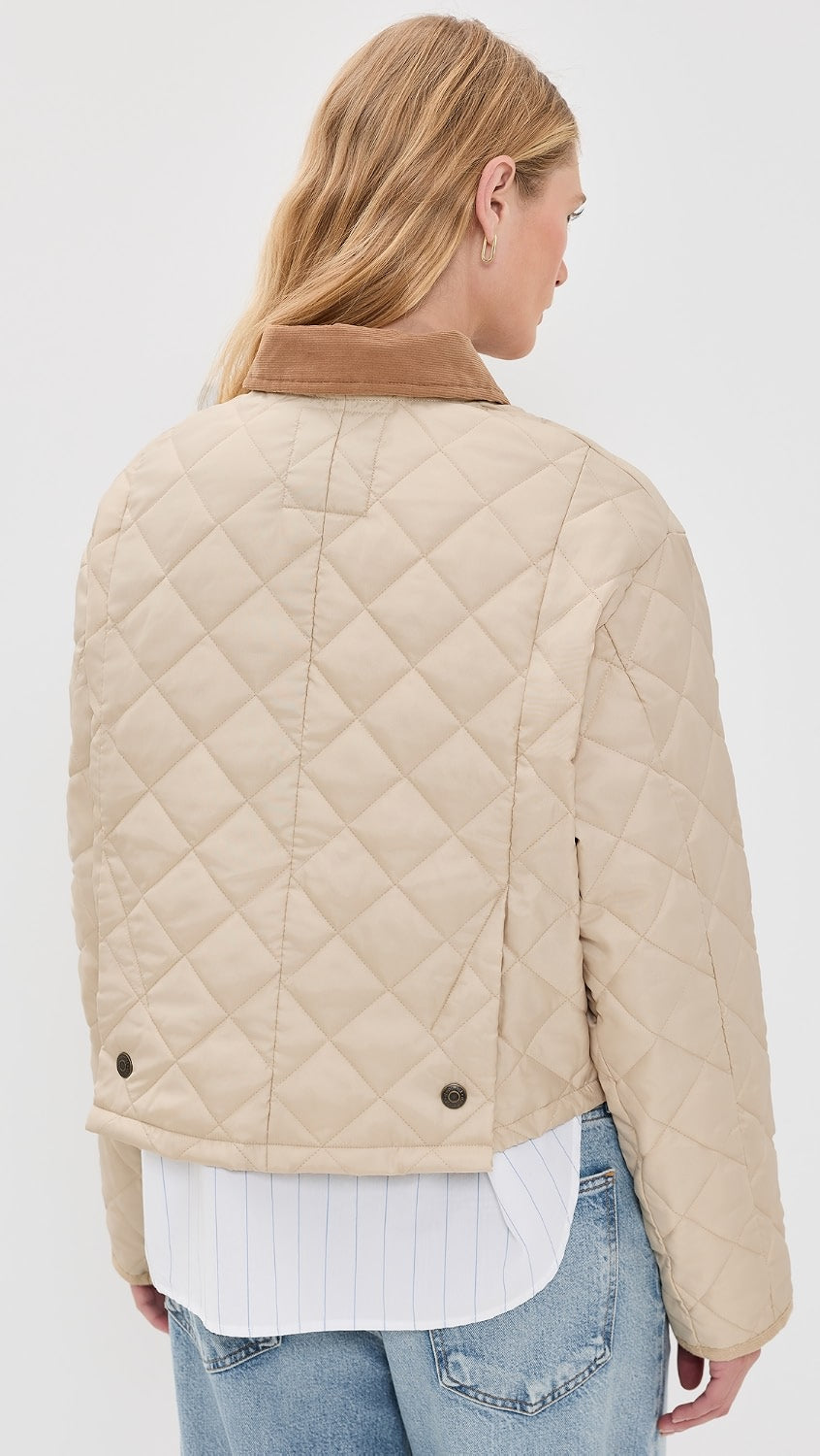 A woman with long blonde hair is seen from behind wearing the Denimist FAULKNER QUILTED JACKET—a beige quilted jacket with snap closure and brown collar—over a white shirt and light blue jeans, set against a plain white background.