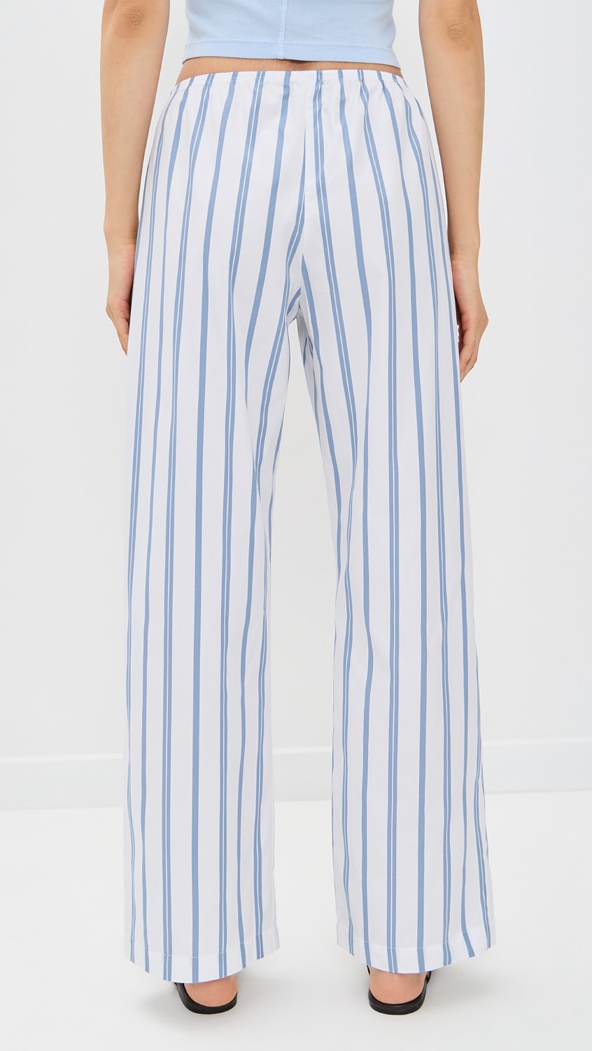 A person faces away from the camera, wearing Donni's The Pop Simple Pant in a high-waisted, wide-leg white poplin stripe style with black heeled shoes against a plain white background.