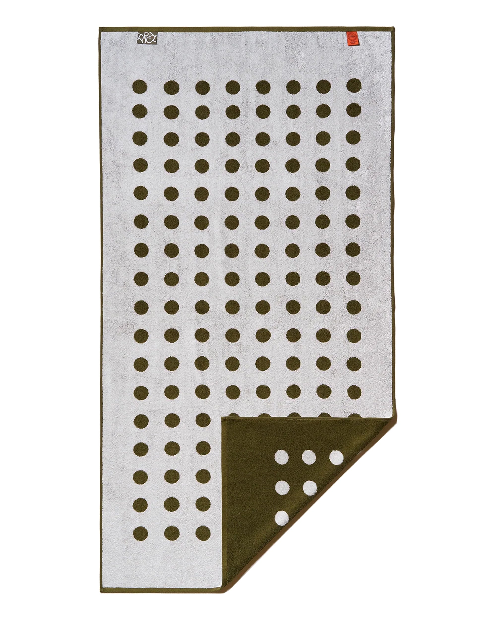 The Typical Moss/Clay Polka Dot Bath Towel is rectangular and reversible, featuring dark green dots on a light gray side and light dots on a dark green side, shown with one corner folded to display both patterns.