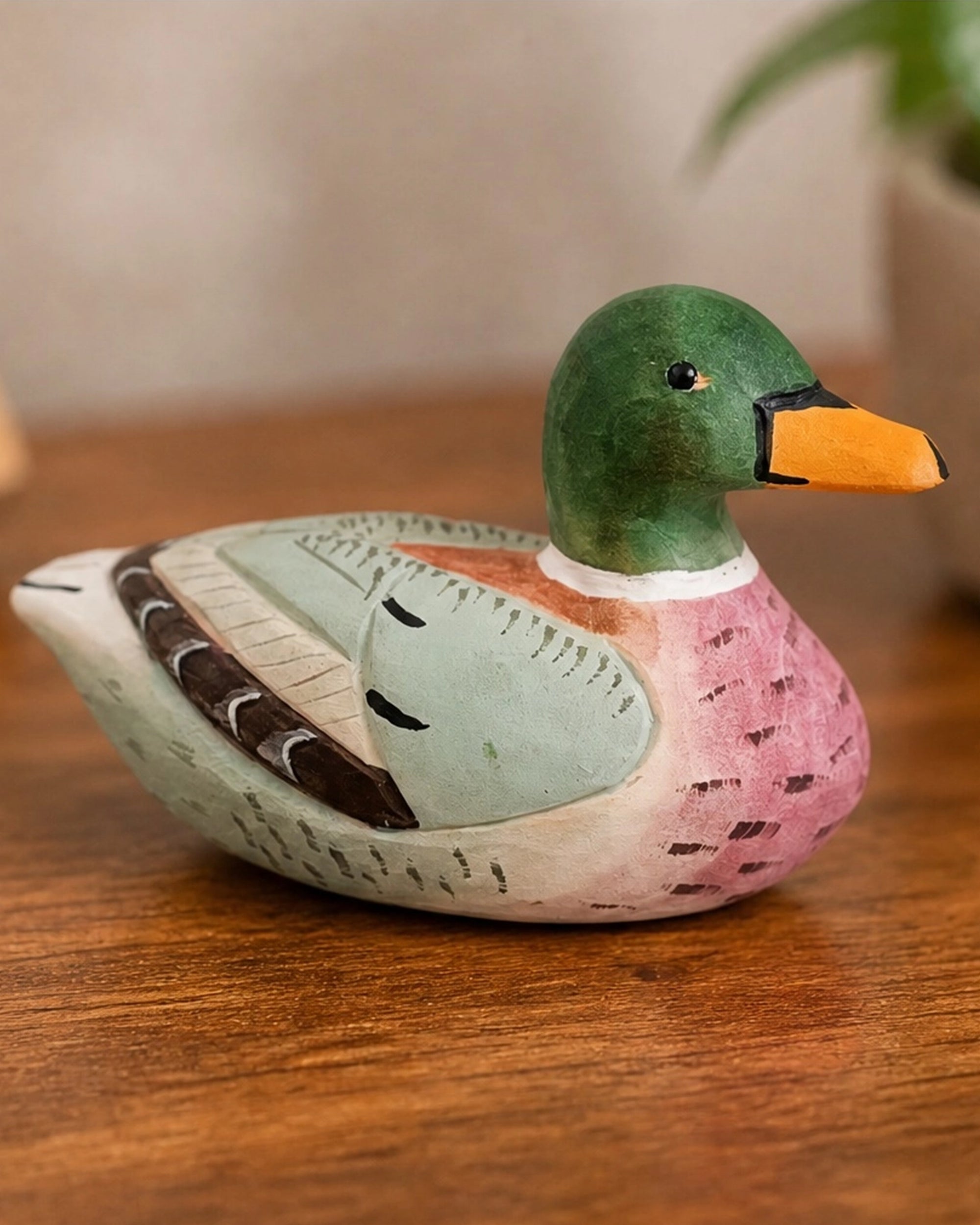 Pink hand-painted carved basswood duck by The Faire on wood with a softly blurred plant background.