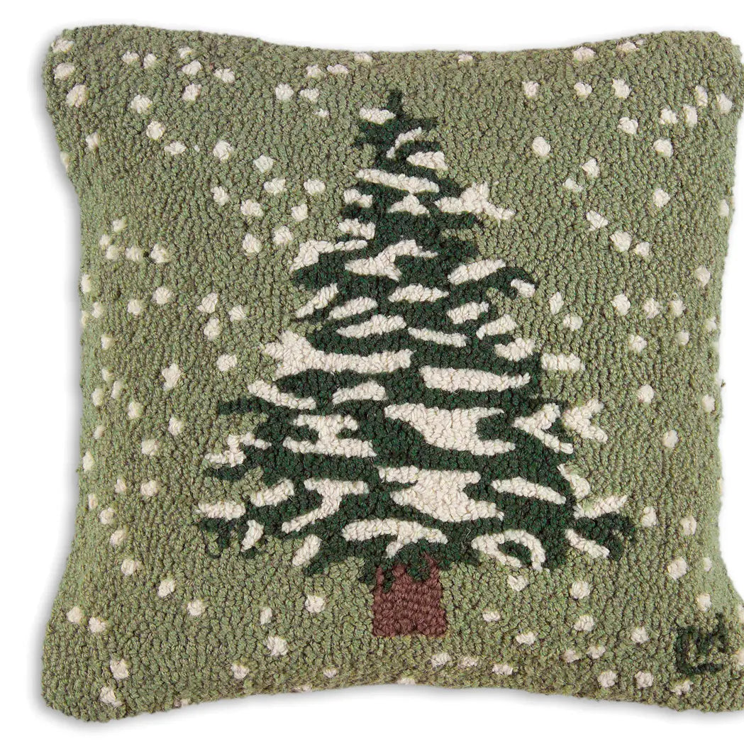 The Faire Christmas Flurries Frosted Tree Pillow is a hand-hooked wool pillow featuring a snow-covered tree and falling snowflakes on green—perfect for cozy holiday decor.