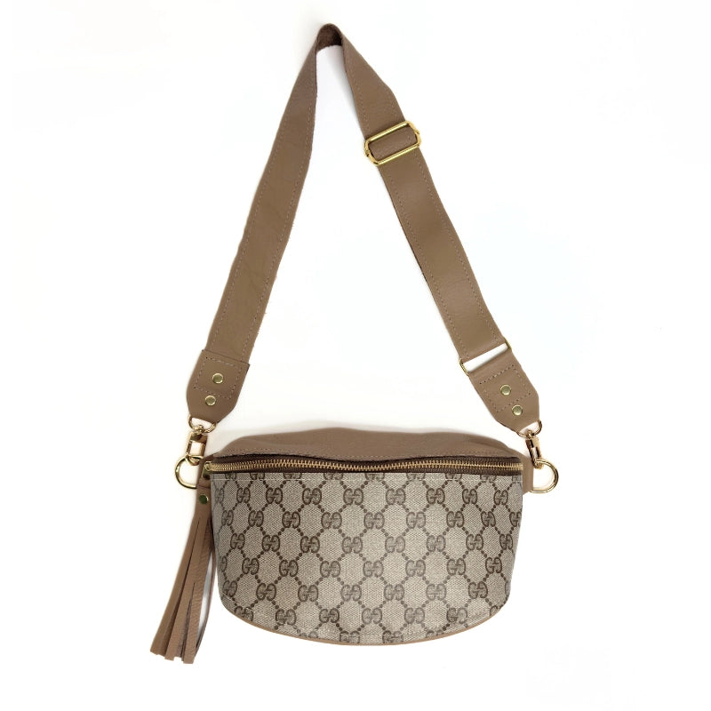 The Britt Belt Bag by Faire is crafted from black leather with an adjustable belt strap, gold hardware, and zipper closure. This designer purse features a sleek silhouette and a decorative detail on the side.