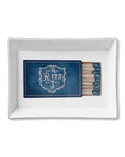 The Faire Ceramic Tray is a rectangular white ceramic trinket tray with a blue matchbook labeled "Paris Ritz Hotel" and matches on the right—ideal for organizing small items or giving as a stylish gift.